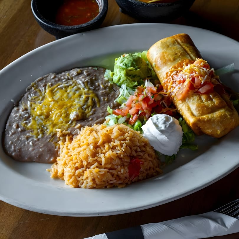 A chimichanga meal with refried beans, rice, guacamole, pico de gallo, and sour cream.