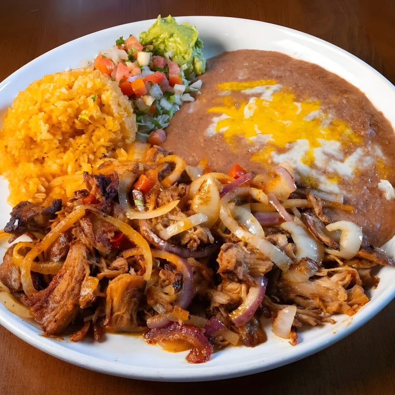 A white plate with Mexican food, including rice, refried beans, guacamole, pico de gallo, and carnitas.